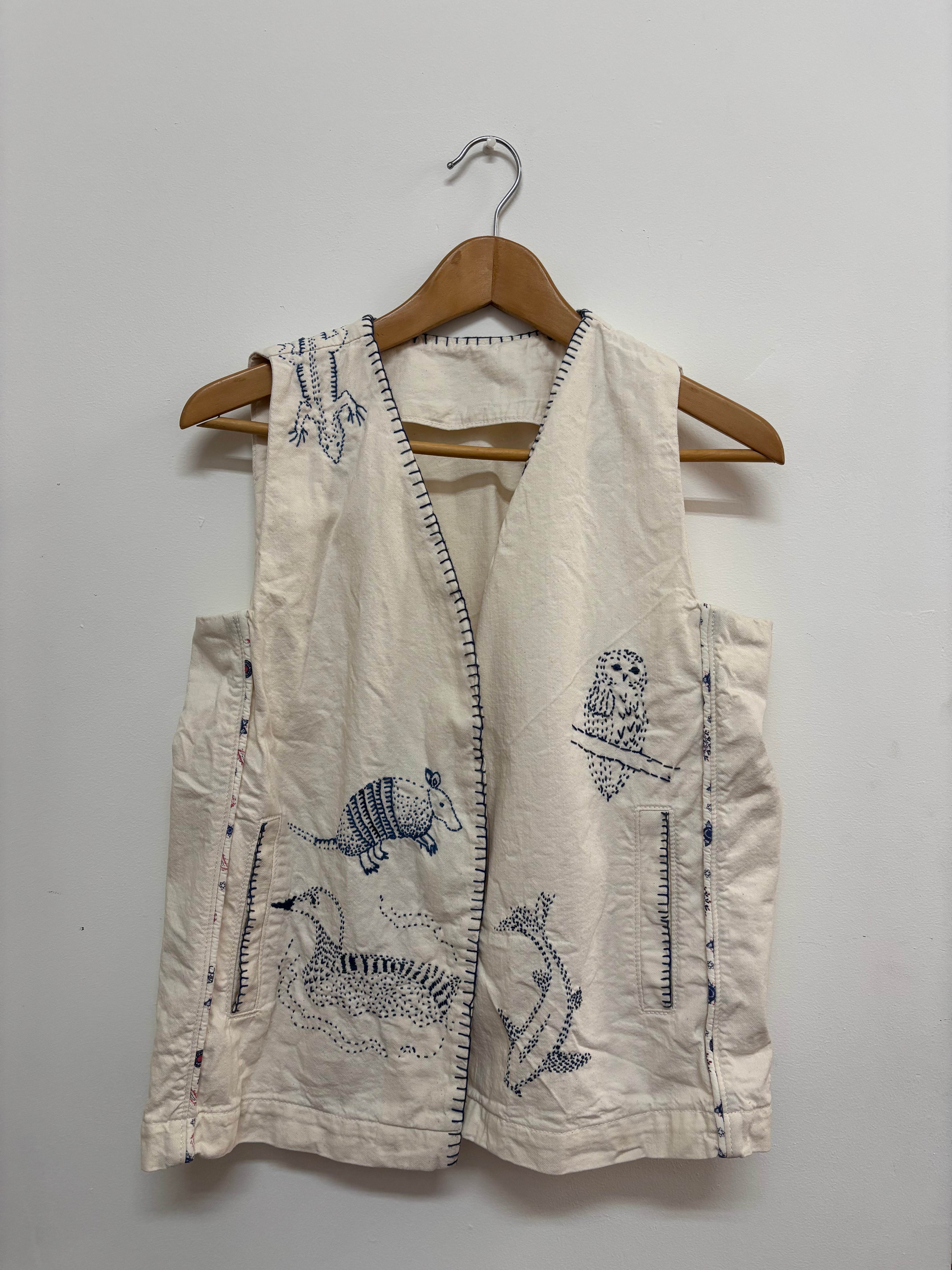 Cream vest with hand-embroidered blue animals including an owl and armadillo
